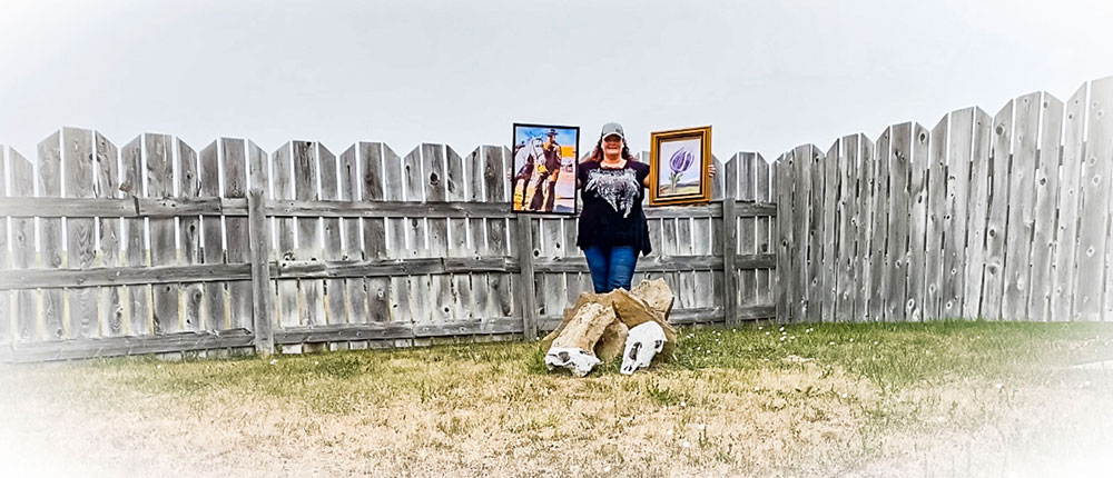 Woman standing in front of a gray fence holding two paintings